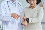 Close-up shot of middle-aged cardiologist standing next to his senior patient and showing her how to use fitness tracker